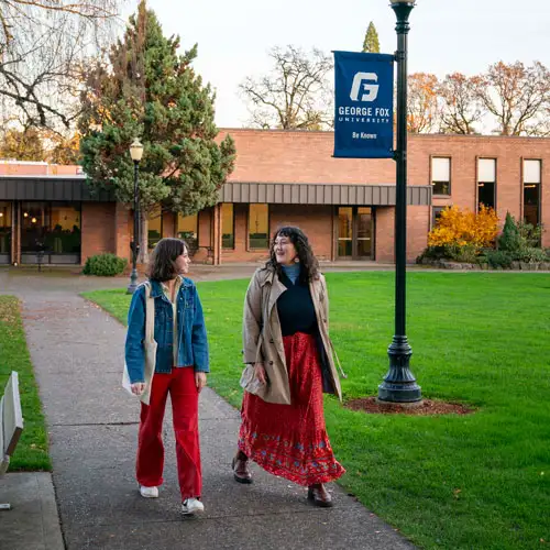 Student walking through the quad and conversing with George Fox faculty