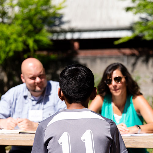 Two counselors listen to a child outside on a lunch bench.