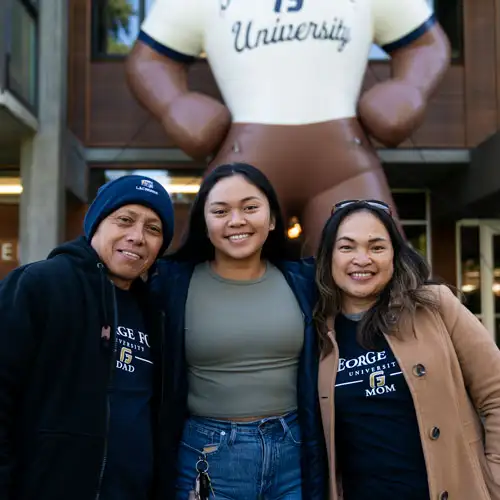 A student smiling in front of Stevens with her arms around her parents
