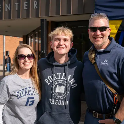 A student standing in front of Klages with his arms around his parents