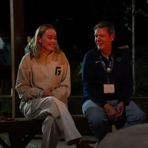 A student sitting next to her dad by a fire at Family Weekend