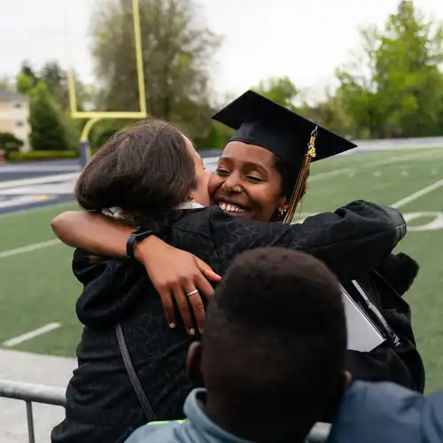 Student in graduation gown hugging a family member