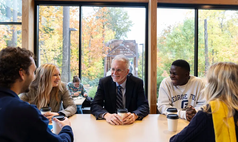 Robin Baker sits at a table with 4 students and listens to them talk
