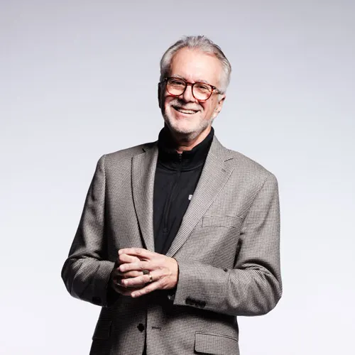 Robin Baker in a gray suit laughs with his hands clasped together