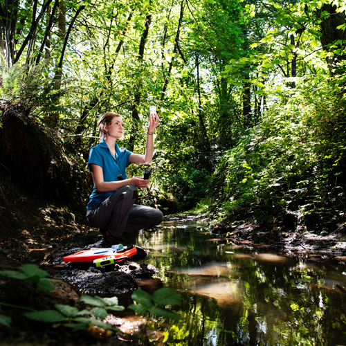 Student kneels down by a creek.