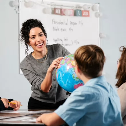 teacher helping a student and pointing at a globe