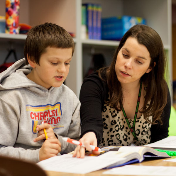 Student and teacher at a table reading a book together