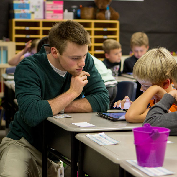 MAT student works in classroom at desk with young students