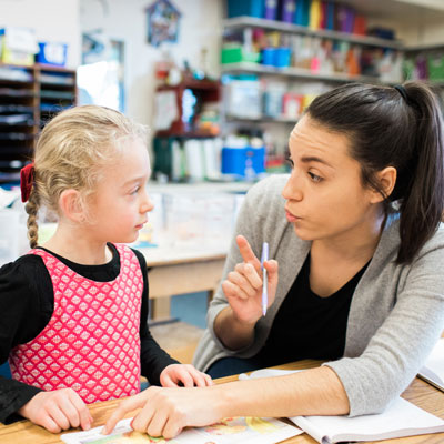 Female teacher points to book and sounds out word for student