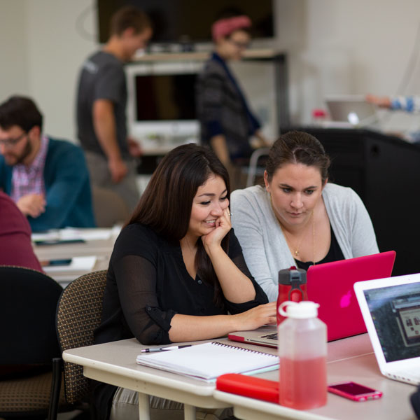 2 students look at a pink laptop in a classroom