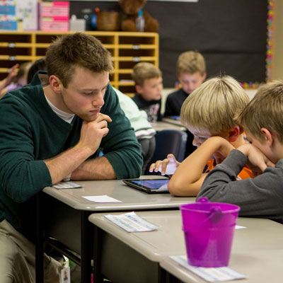 Mat student at desk with young children learning to read