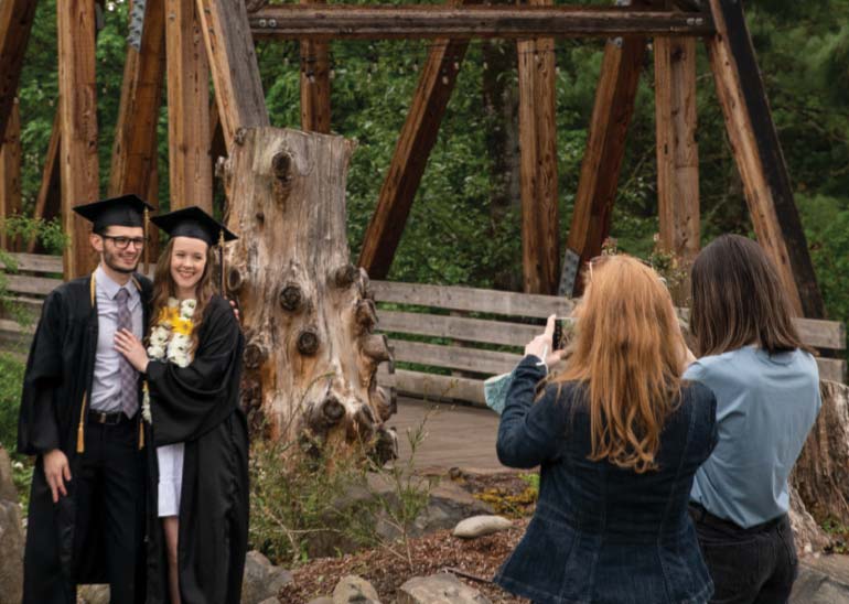 A male and female student pose for a photo by the Crisman Crossing bridge on campus