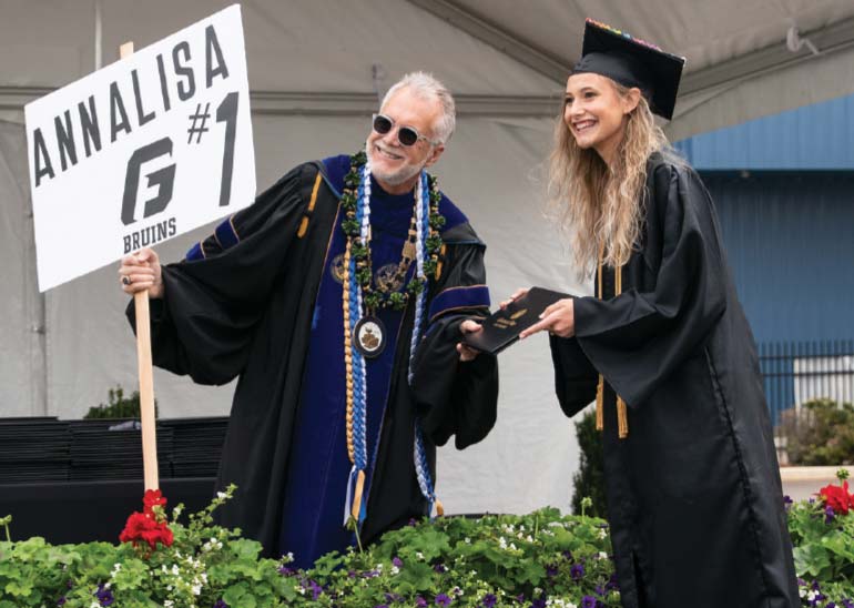 President Robin Baker hands a degree to a student, while holding a handmade sign that reads 'Annalisa #1'