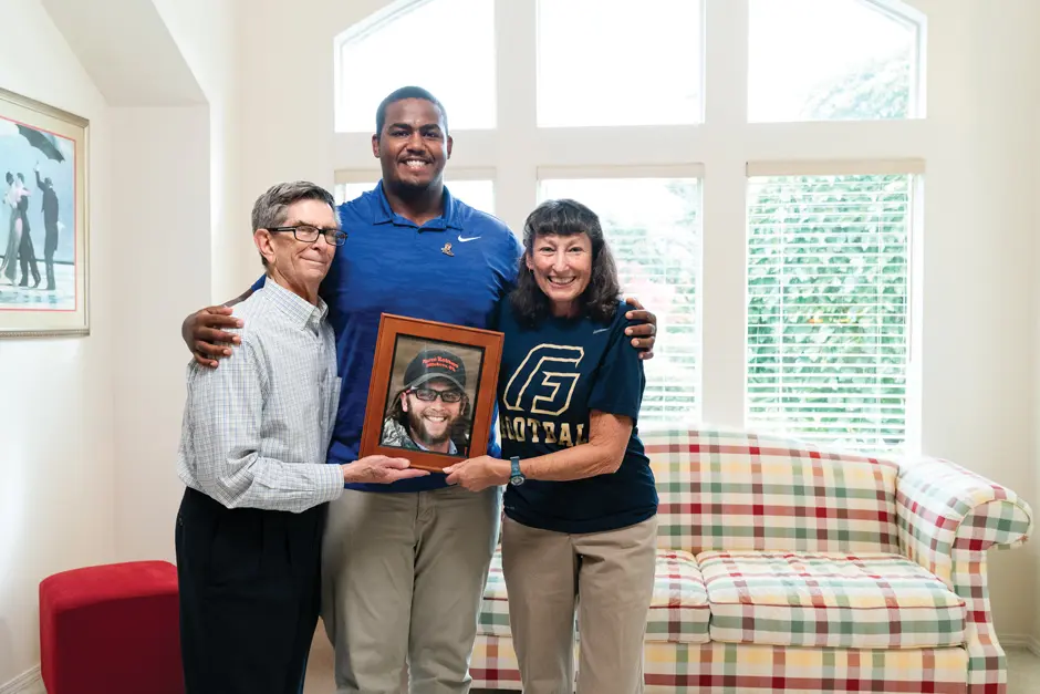Zach Luworo standing with his arms around Joe and Nadine Kincaid who are holding a framed picture of Kyle Kincaid