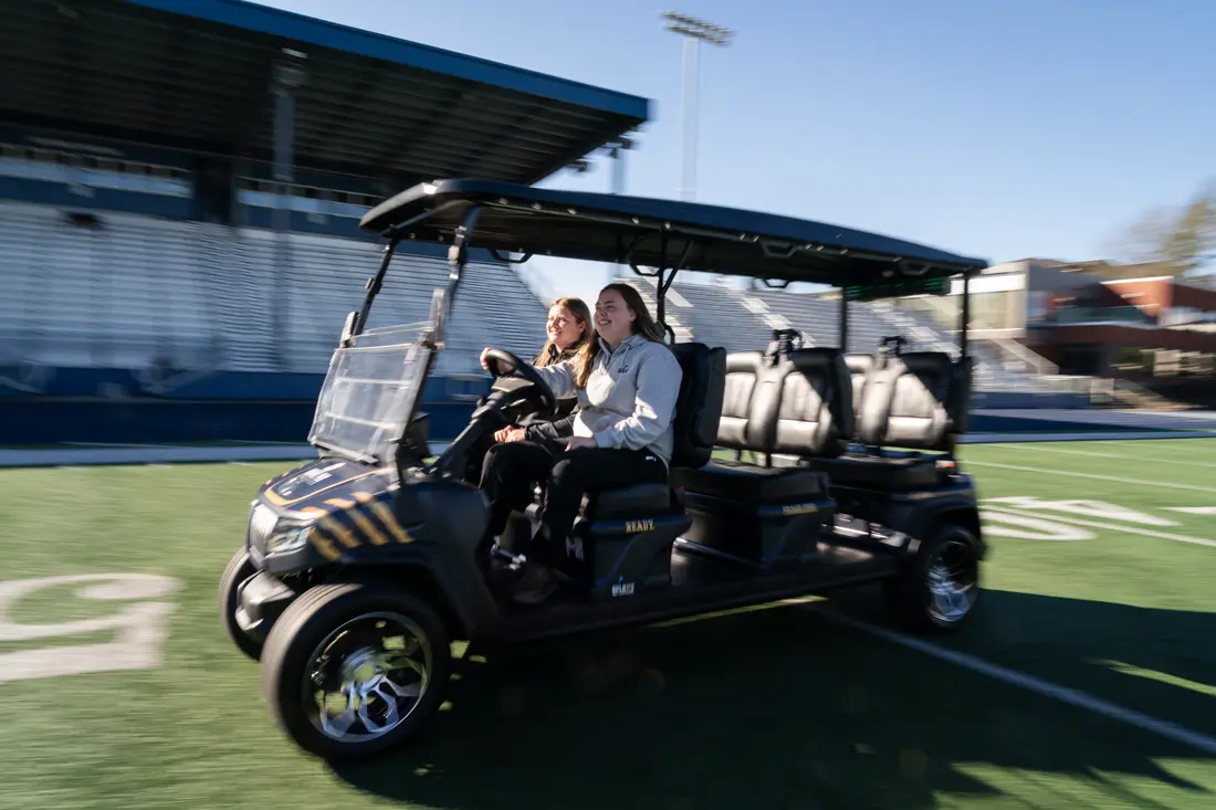 Jensyn Lown and Demi Guild taking a golf cart for a spin around the football field with big smiles on their faces