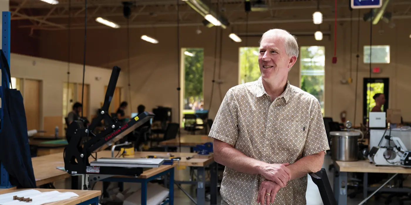 Neal leaning against a bench while smiling proudly in the George Fox Maker Hub