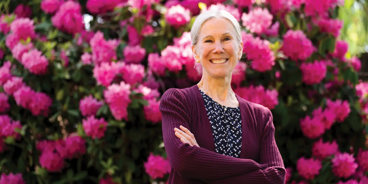 MaryKate Morse standing and smiling proudly in front of a bush of pink flowers