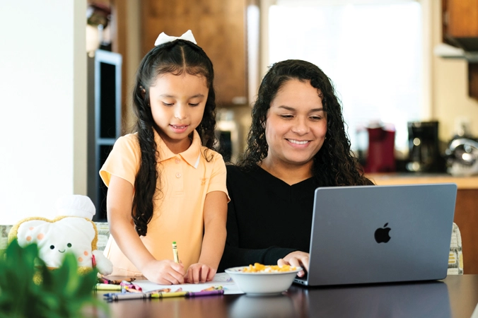 Mother doing homework on her computer while her daughter plays nearby