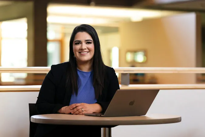 Nathalie sits at a round table with her laptop and smiles at the camera