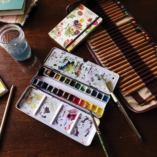 Christine Joy's work table with water color paints and colored pencils