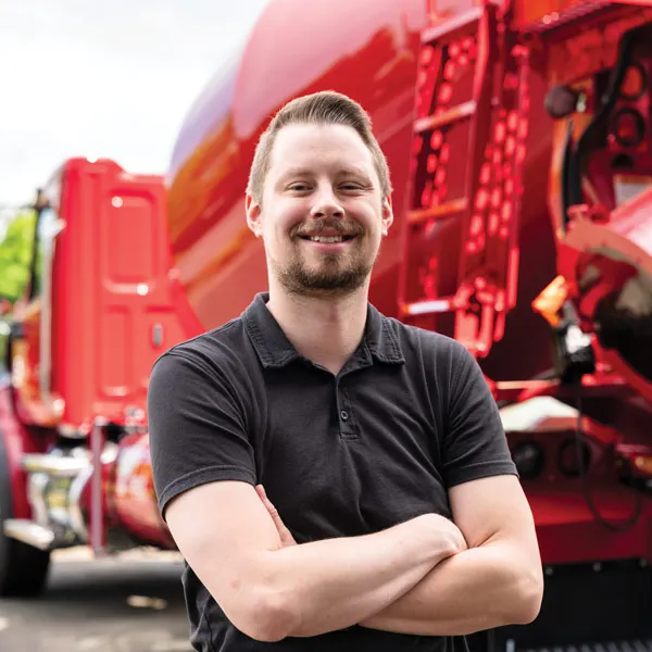 A man is standing next to a large red truck. 