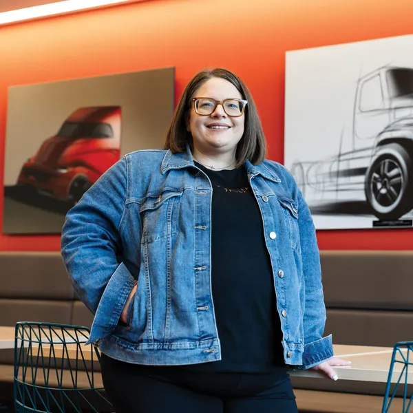 A woman in a blue jacket and black shirt is standing in a room with two pictures of trucks on the wall.