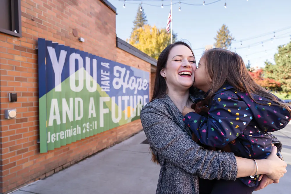 Tia holds her daughter and laughs in front of a sign on campus that reads, "You have a hope and a future"