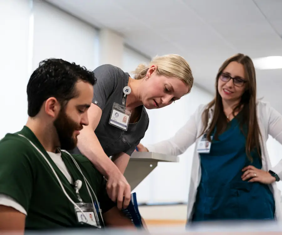 CRNA student applies a blood pressure cuff to her peer while Professor Wendy Morley gives instruction