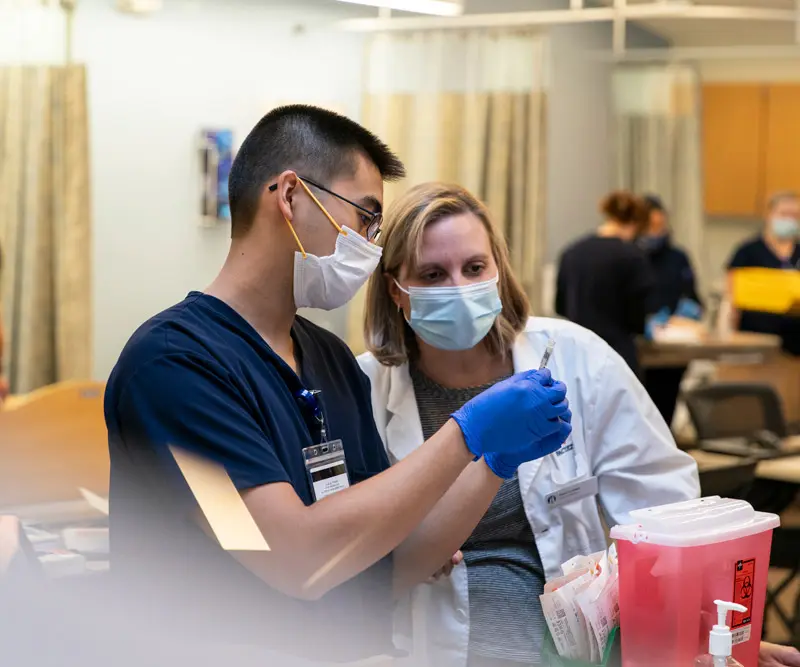 Professor helps a CRNA student with a syringe