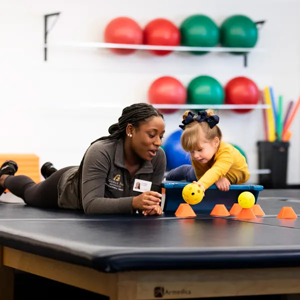 A George Fox University OT student works on motor skills with a young girl with a ball