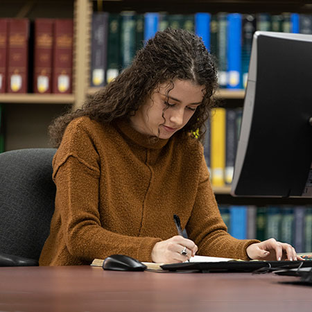 A student writing notes while sitting in front of computer