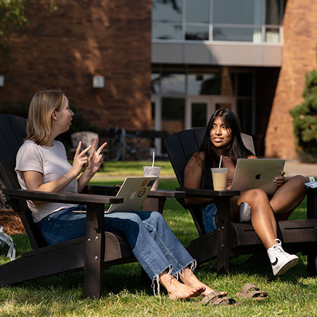 Two students having a conversation sitting outside on campus quad