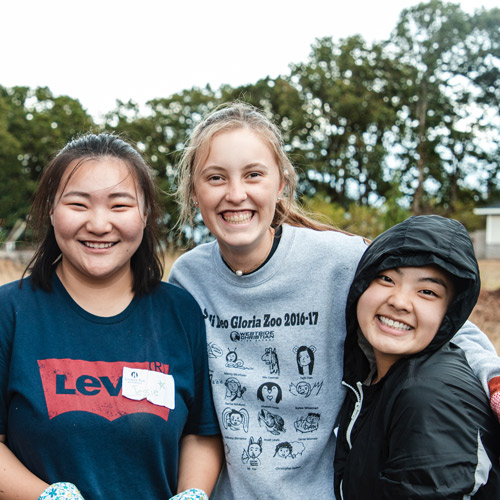 3 students smile together outside