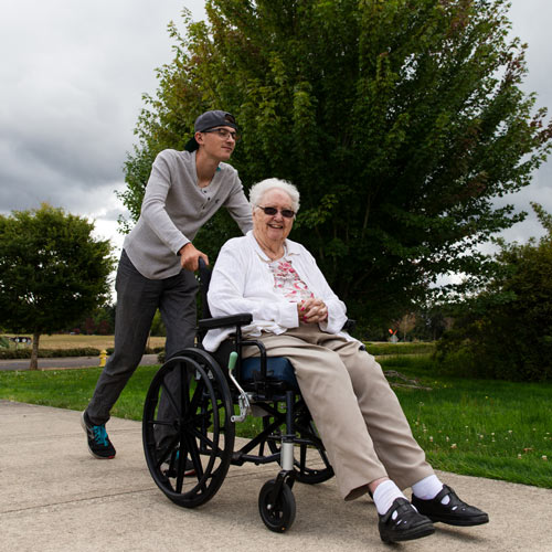 Students walks with older individual in wheelchair