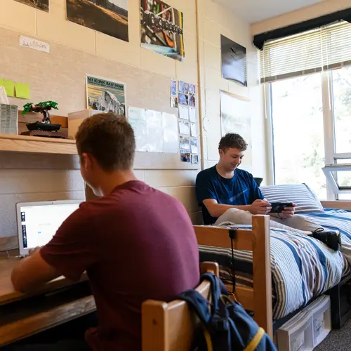 Two friends studying and playing a video game in their dorm
