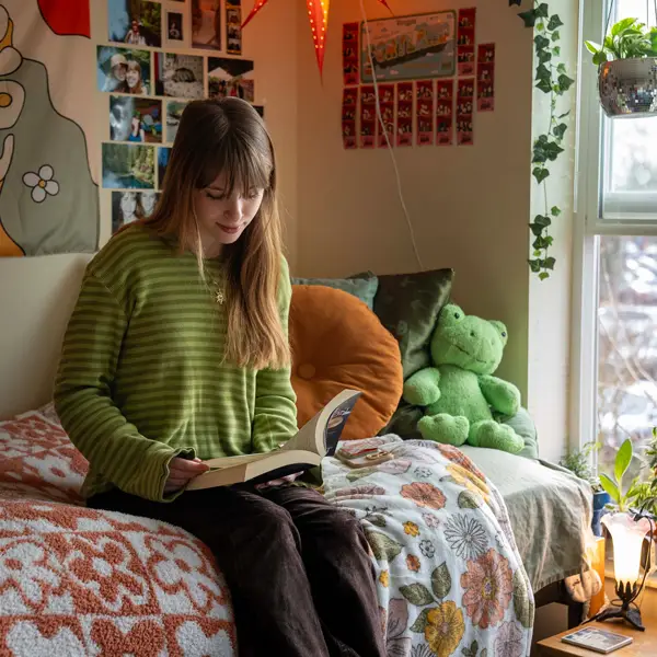 Grace reading a book on her bed in her hippy bohemian style dorm