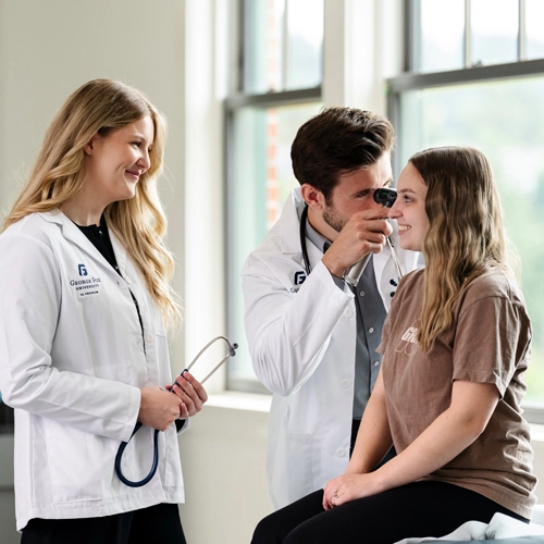 One PA is checking a patient's ear canal, while another PA stands nearby observing