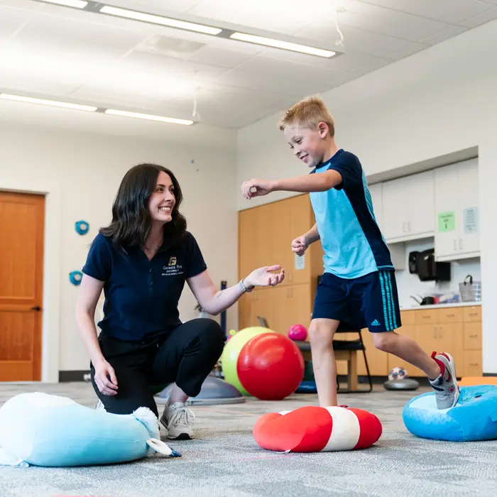 DPT student joyfully coaches a kid to jump along bean bags