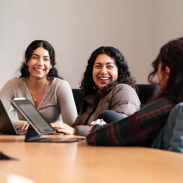 3 female students laugh and talk while working on classwork