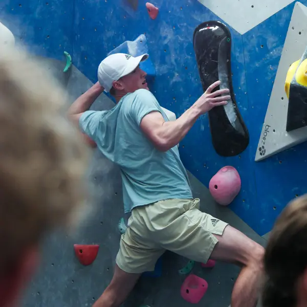student in baseball cap very focused and tense while climbing close to the wall