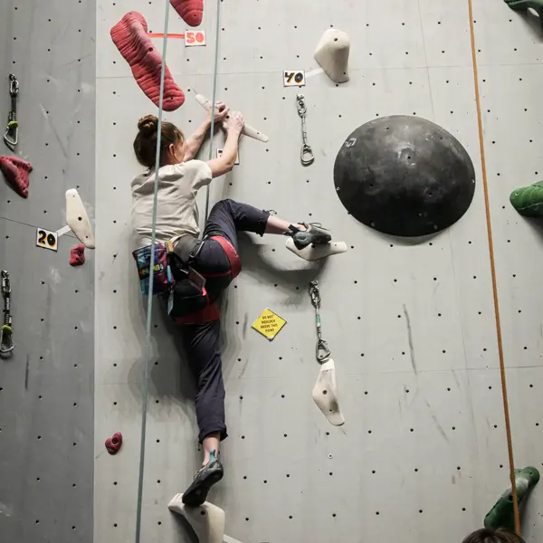 student on ropes holding onto a crimp reaching her leg up the wall to climb