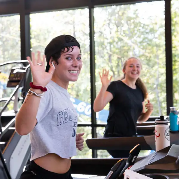 Two girls waving at the camera from treadmills