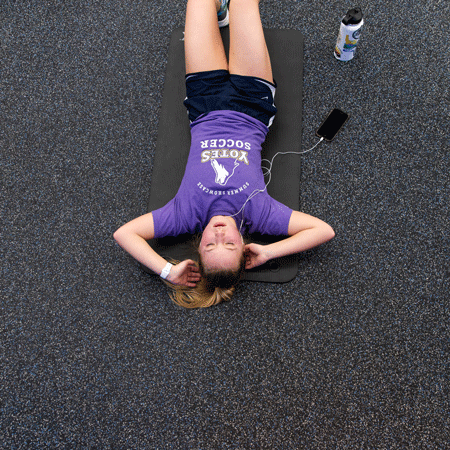 A female student listens to headphones while doing sit-ups in the training room.