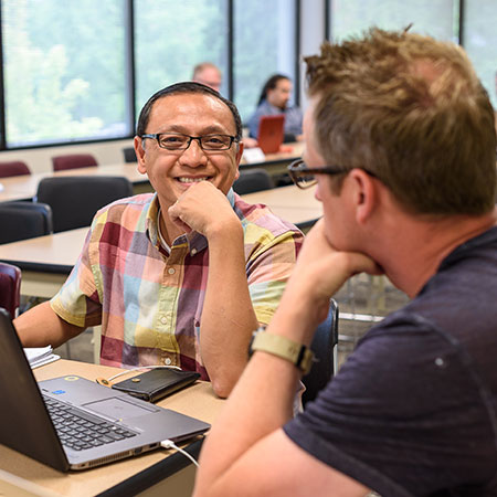 Two seminary students smiling and having a conversation in class