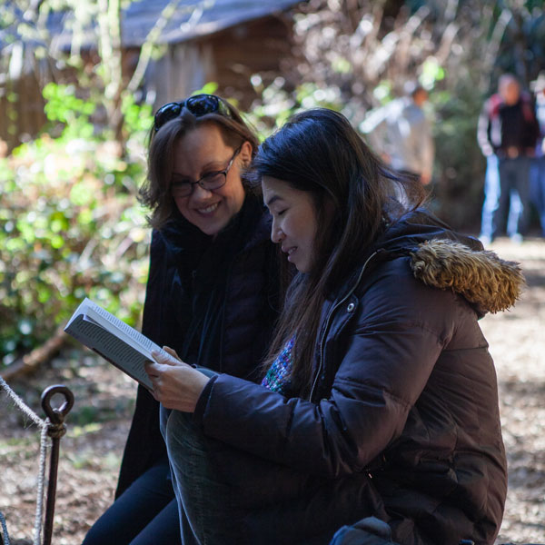 two women read a book outside together