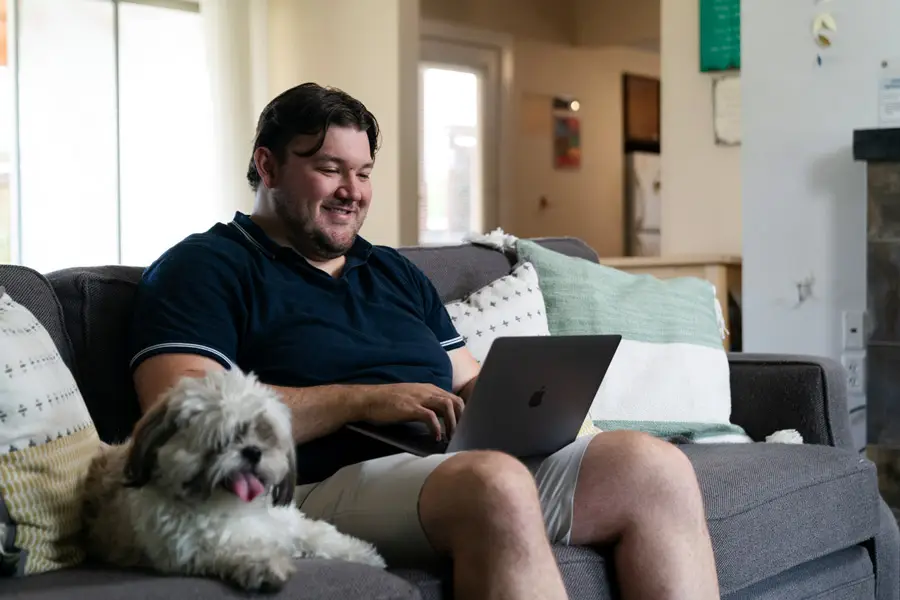 Student works on a laptop on his couch with his dog