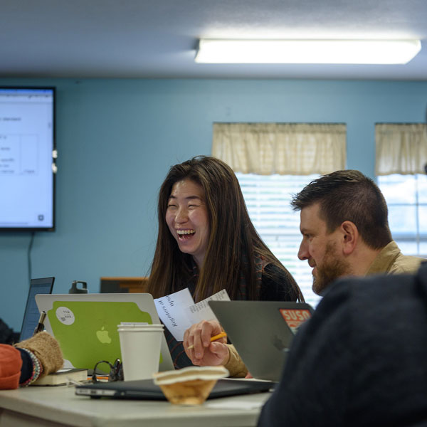 Three students sitting at a long desk on their laptops in class