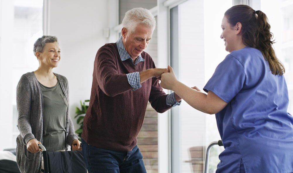 Woman helping an older man stand up from a wheelchair