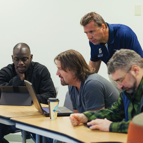 Professor works with 3 adult students in a classroom